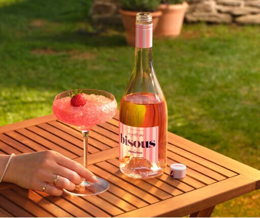 Frose cocktail op een houten tafeltje met een fles Bisous ernaast